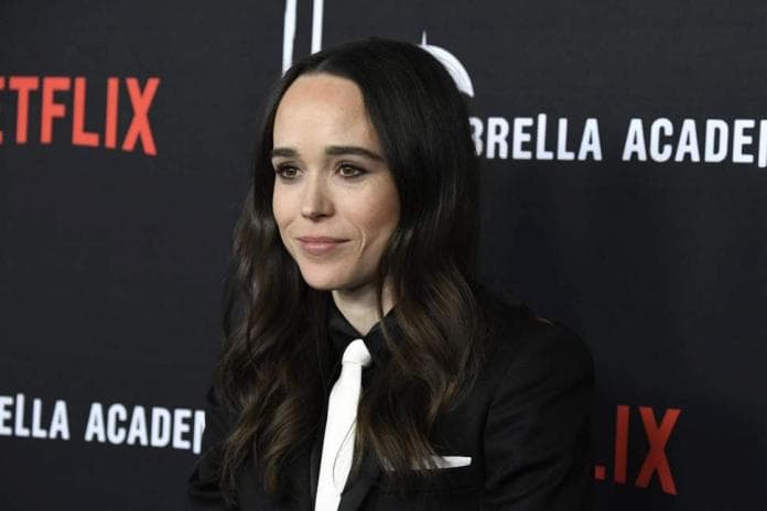 Ellen Page, mulher branca de 31 anos, veste terno preto e gravata branca. Seus cabelos de costanha escura estão ondulados e soltos 