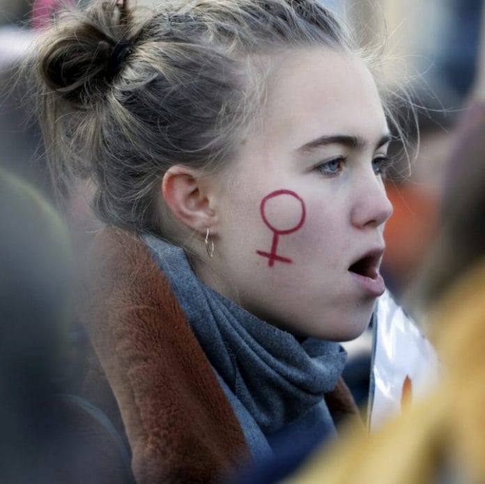 - Mulher em protesto com o símbolo feminista pintado de vermelho no rosto