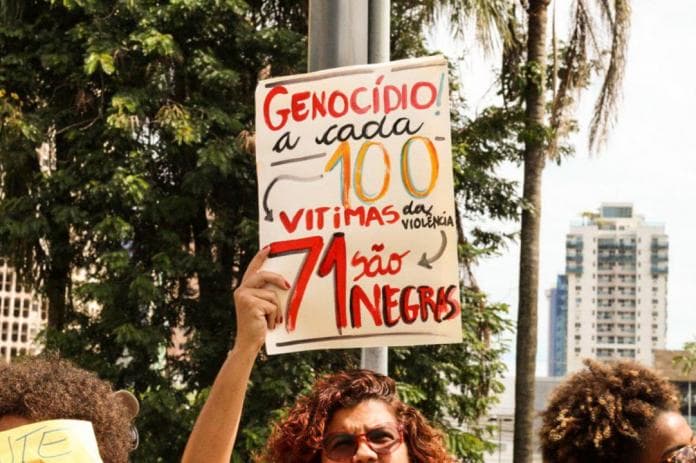 Mulher segurando cartaz com dizeres: Genocídio: a cada 100 vitimas da violência 71 são negros"