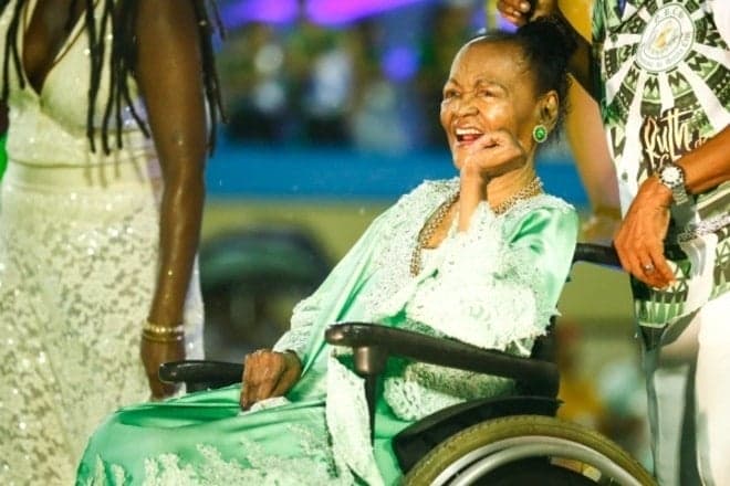 Ruth de Souza, mulher negra idosa, sentada em uma cadeira de rodas na Sapucaí 