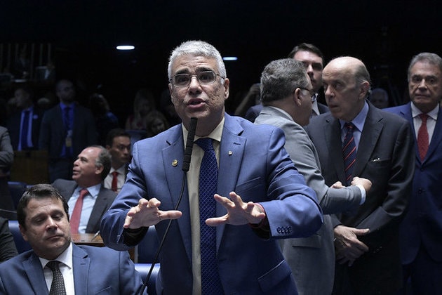 Senador Eduardo Girão, homem branco, 46 anos, de cabelos grisalhos, terno e gravata azul esccuro e camisa marrom clara. O senador está em pé, falando no microfone 