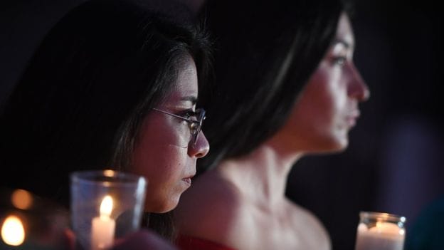 Imagem focando o rosto de duas mulheres, brancas de cabelos compridos e preto, segurando velas em suas mãos