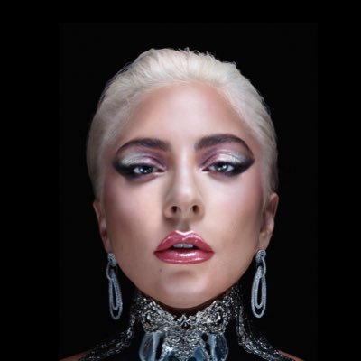 Foto mostrando apenas o rosto de Lady Gaga- mulher branca de cabelo platinado, usando brincos grandes.