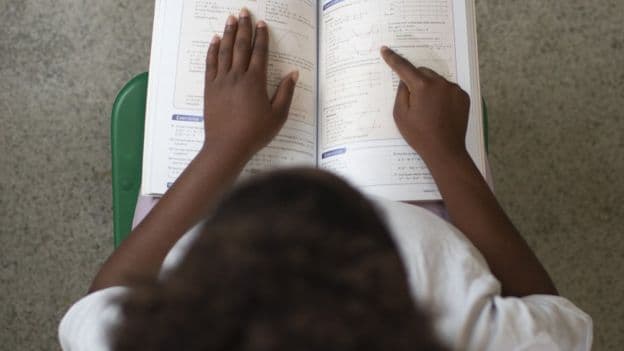 Foto d=vista de cima de uma menina lendo um livro de matemática 