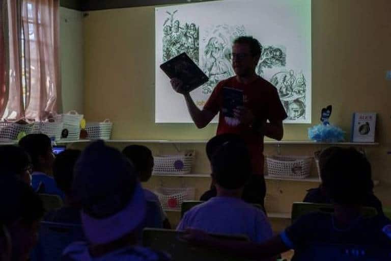 Foto de um professor dando aula em uma sala pouco iluminada 