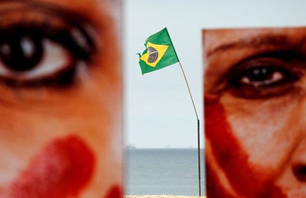 Foto de metade do rosto de duas mulheres com tinta vermelha no rosto e uma bandeira do brasil entre elas 