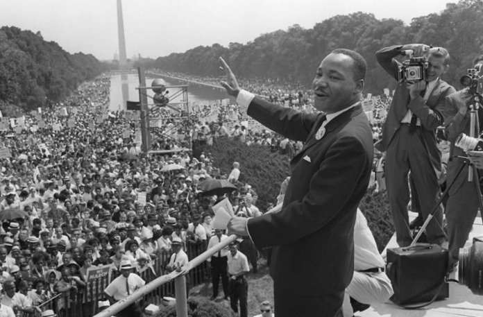 Martin Lither King Jr- homem negro, de pouco cabelo, vestindo terno e gravata- acena a seus seguidores que o acompanhava na marcha de Washington onde fez o seu mais famoso discurso 28.ago.1963 