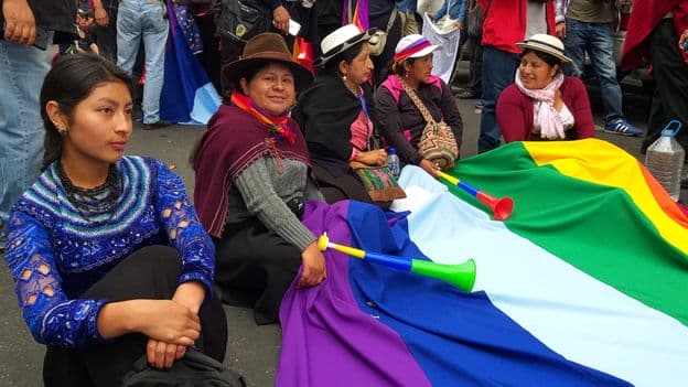 Imagem de muheres sentadas no chão segurando a bandeira do Equador 