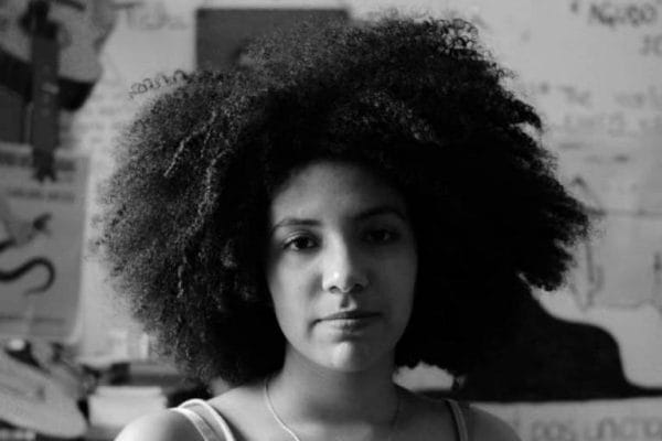 Foto em preto e branco de Letícia Chagas - mulher negra de cabelo crespo- olhando para frente 