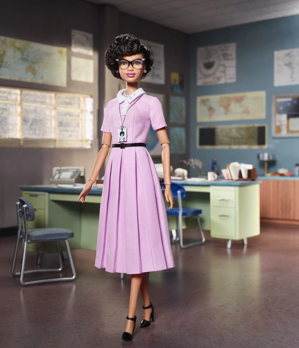 Barbie inspirada na cientista Katherine Johnson- boneca negra, usando óculos e vestido longo e rosa 