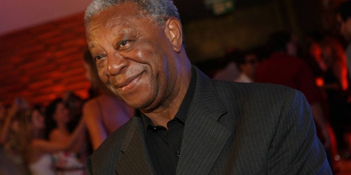 Milton Gonçalves - homem idoso negro, de cabelo curto e grisalho, vestindo terno - em pé sorrindo 