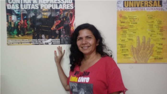 Neila Gomes - mulher de cabelo cacheado, usando camiseta vermelha escrito "Lula Livre''- em pé apoiada na parede 
