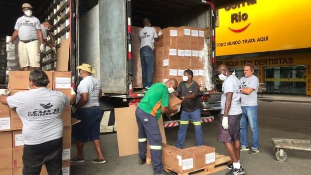 Foto de dois caminhões cheio de caixas sendo descarregados 