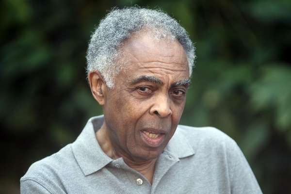 Foto de Gilberto Gil- homem idoso negro, de cabelo grisalho, vestindo camiseta cinza- sentado olhando para o lado 