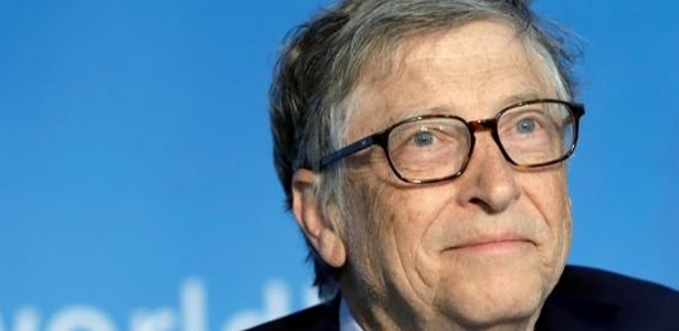 Rosto de Bill Gates em um fundo azul claro .Bill Gates é um senhor de cabelos grisalhos, usa óculos , olhos azuis e pele branca #PraCegoVer